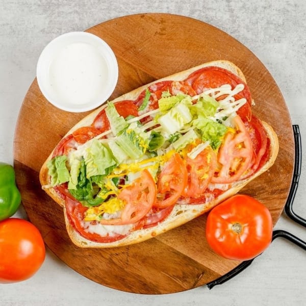South Lake Pizza sub sandwich with pepperoni, lettuce, tomatoes, and sauces on a wooden board.