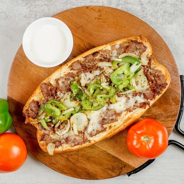 South Lake Pizza's cheesesteak sub with green peppers, onions, and melted cheese, served with a side of sauce.