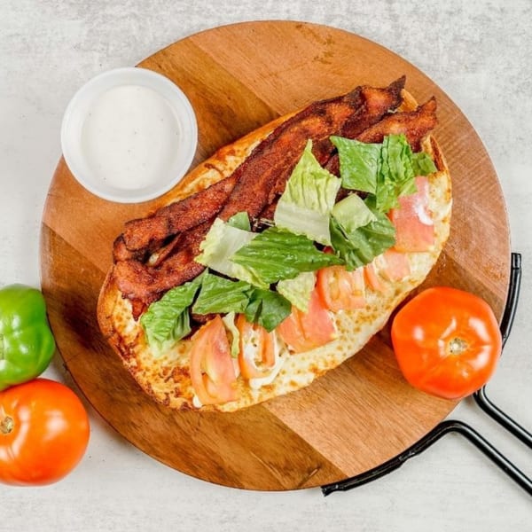 A South Lake Pizza BLT sandwich with bacon, lettuce, tomato, and dressing on a wooden board.