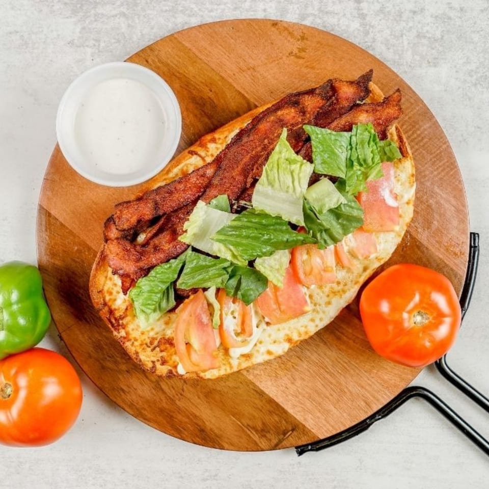 A South Lake Pizza BLT sandwich with bacon, lettuce, tomato, and dressing on a wooden board.