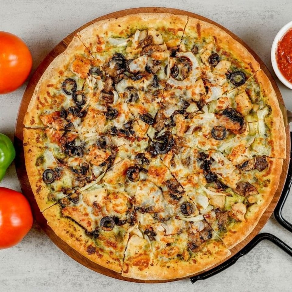 A South Lake Pizza with chicken, olives, mushrooms, and onions on a wooden board.