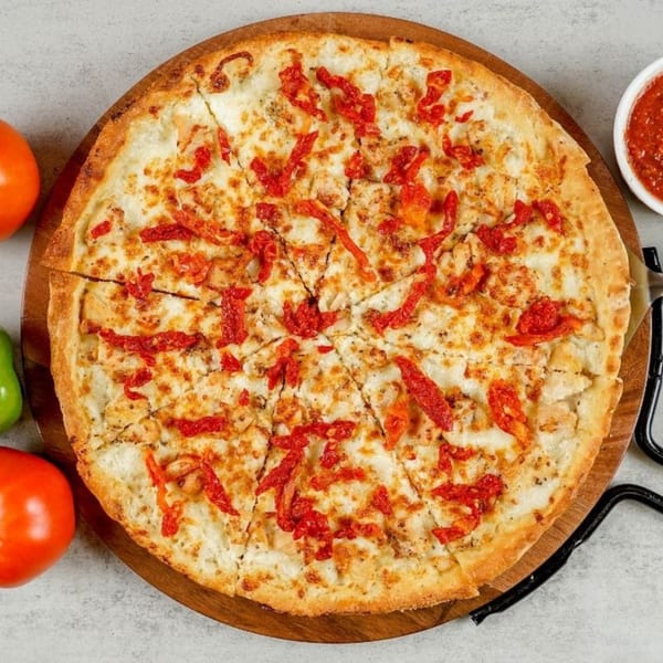 A South Lake Pizza chicken pizza with sun-dried tomatoes, served on a wooden board.
