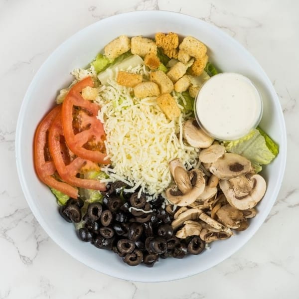 A fresh garden salad with lettuce, tomatoes, olives, mushrooms, shredded cheese, croutons, and dressing.